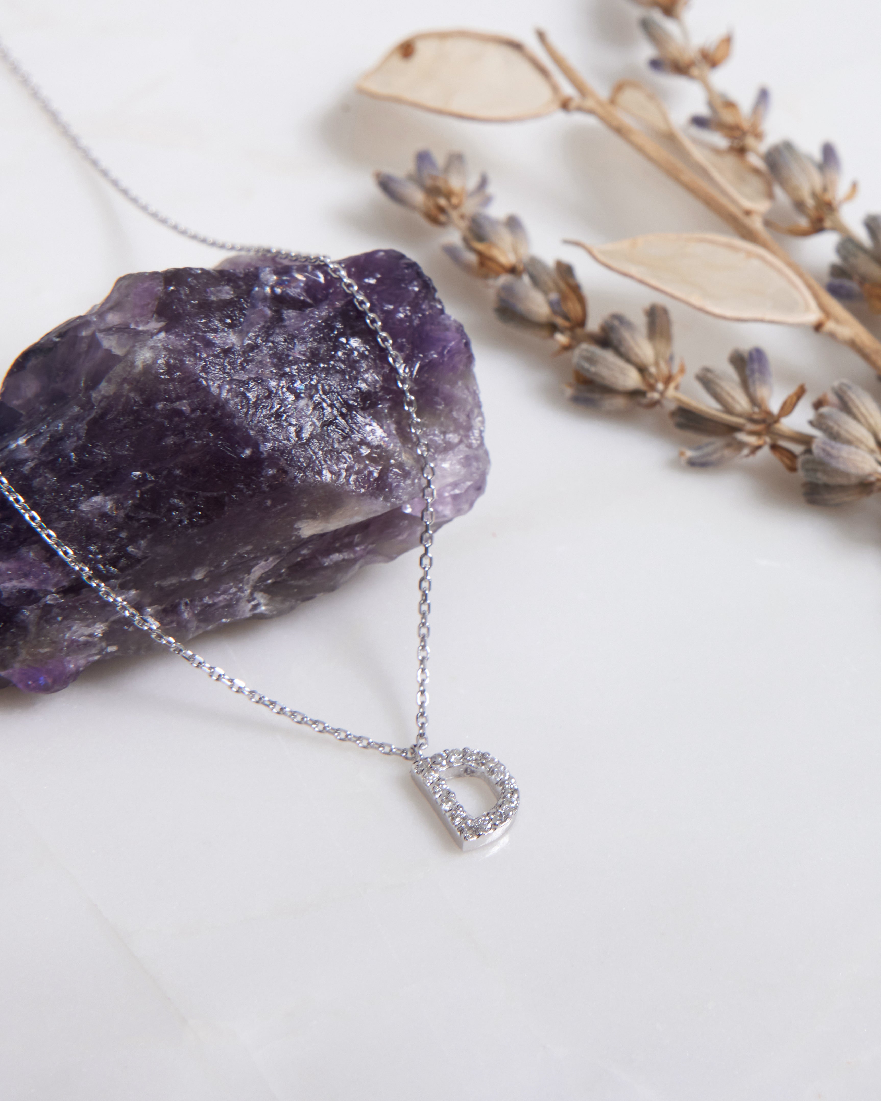 14K white gold diamond initial necklace with letter D, resting on amethyst stone and dried flowers.