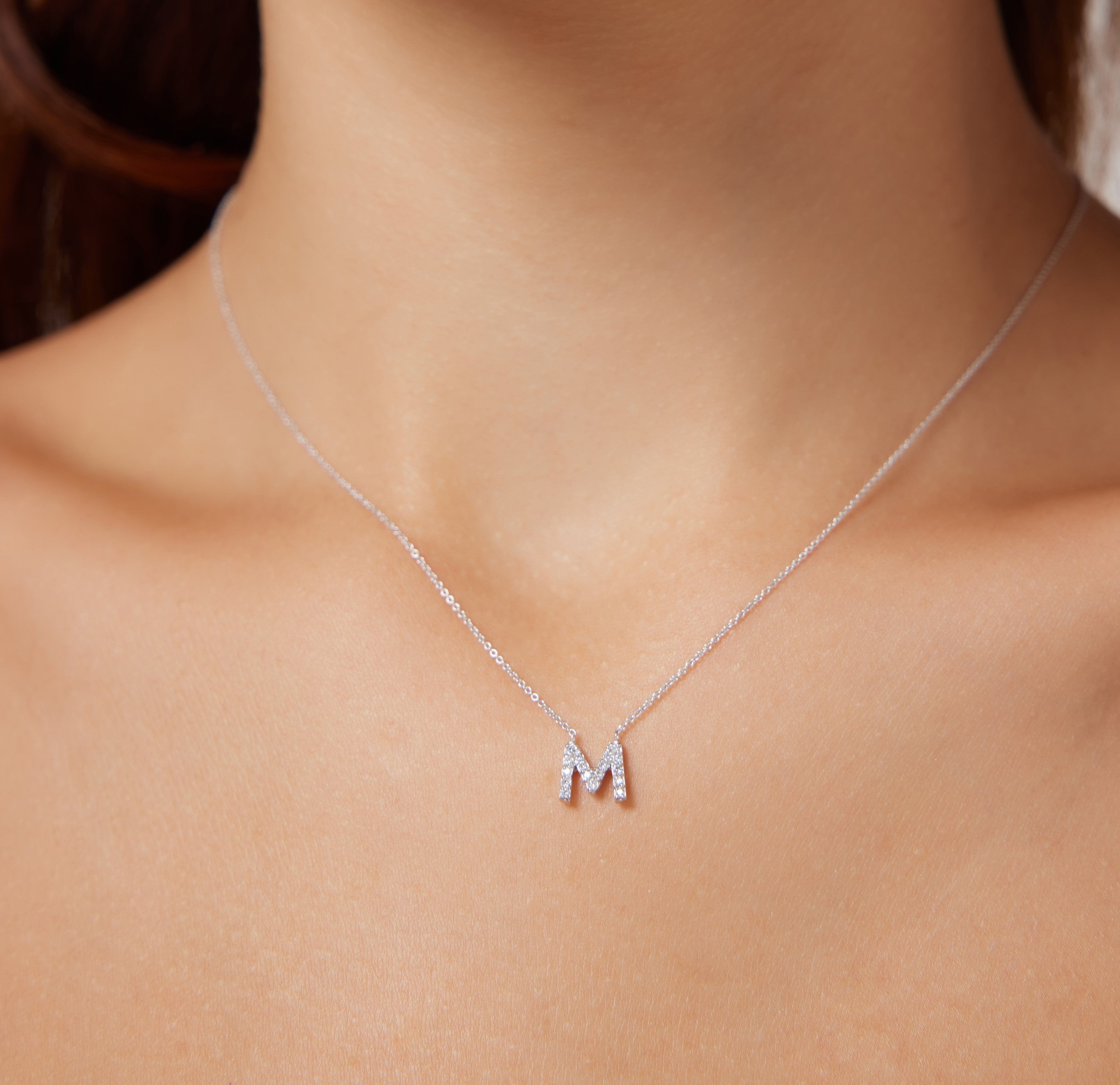14K white gold diamond initial necklace featuring the letter M, showcased on a model's neck.