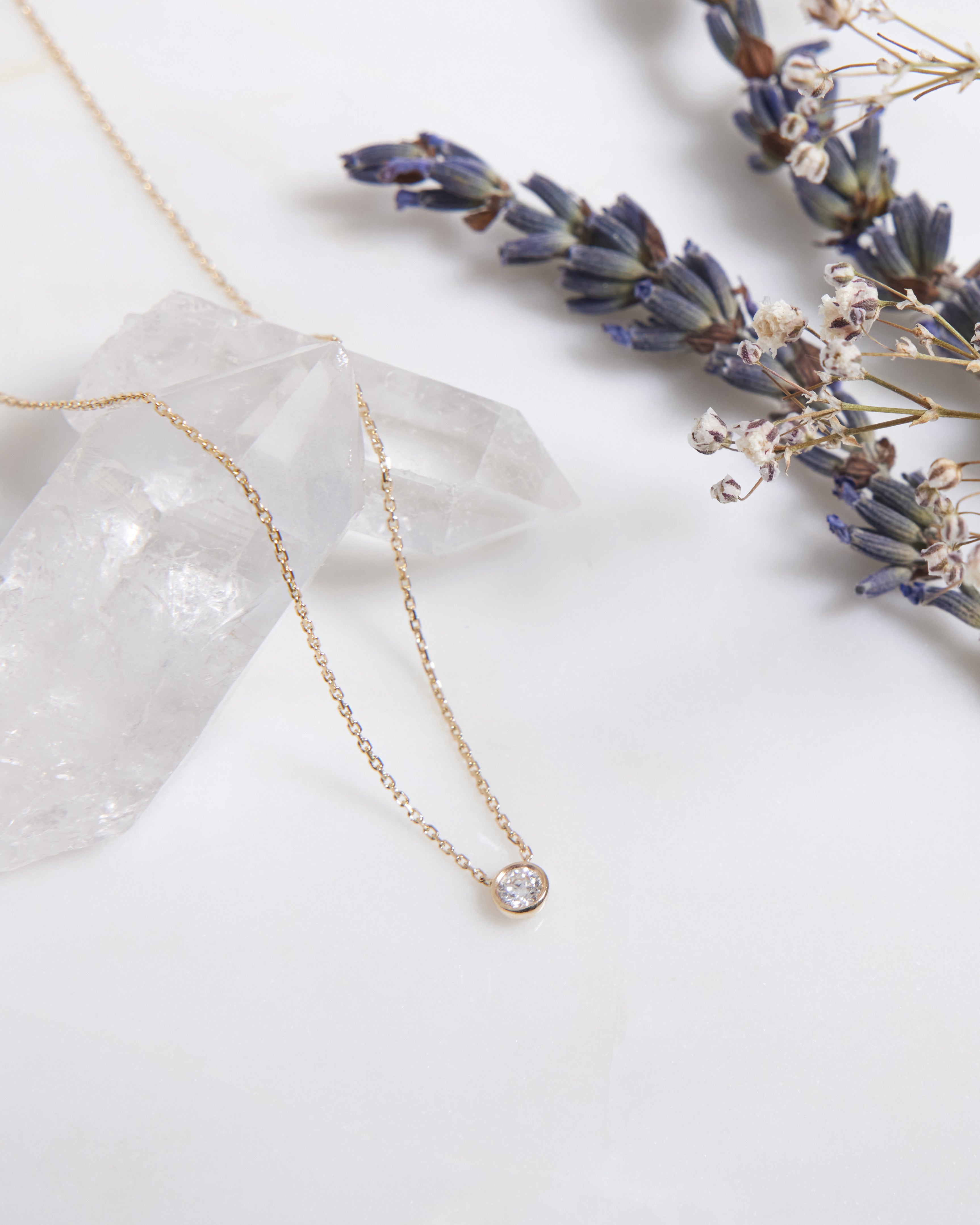 14K solid yellow gold diamond solitaire necklace with a natural diamond, styled with lavender and quartz crystals.