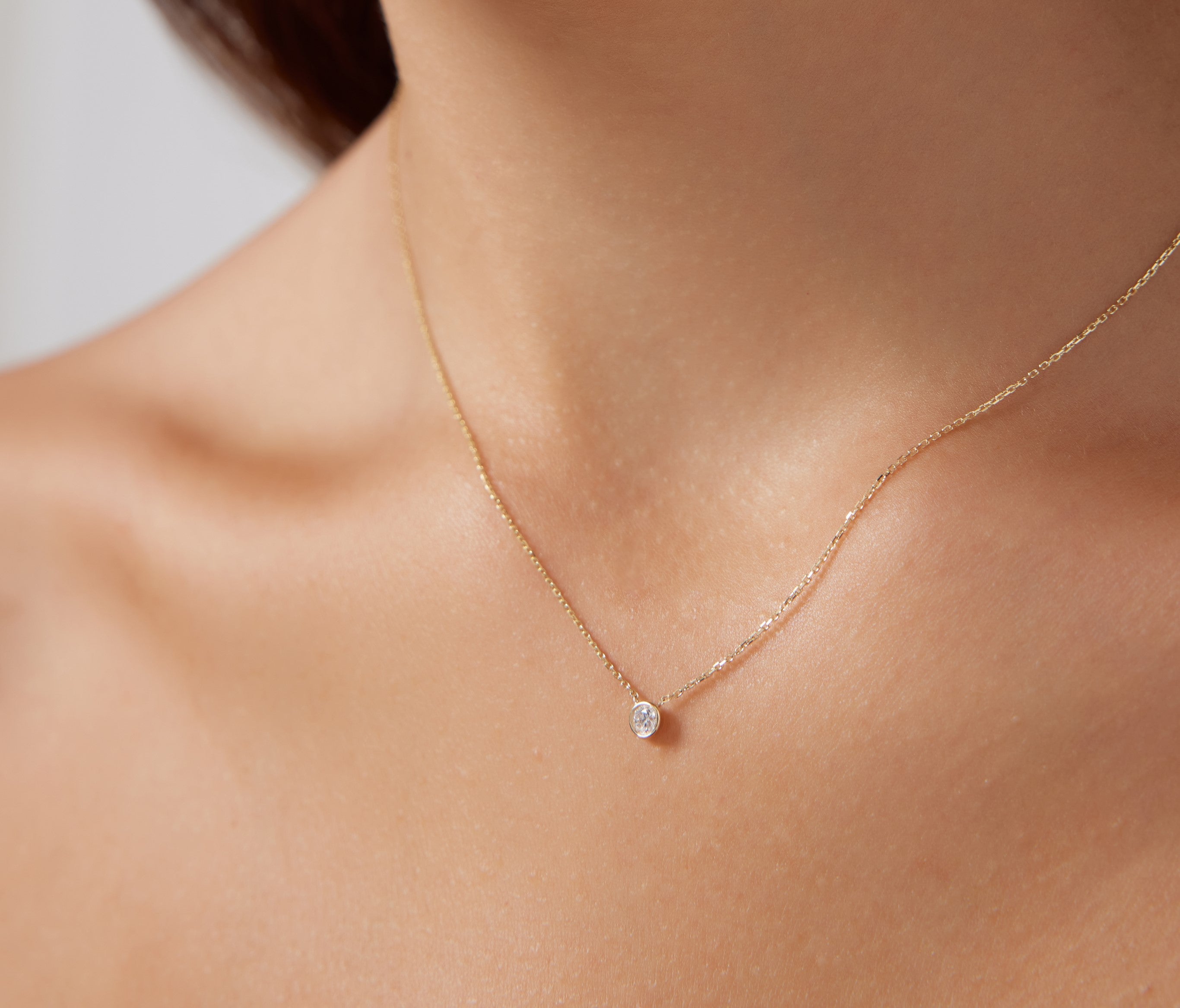 Dainty 14K solid yellow gold minimalist bezel set diamond solitaire necklace worn on a neckline.