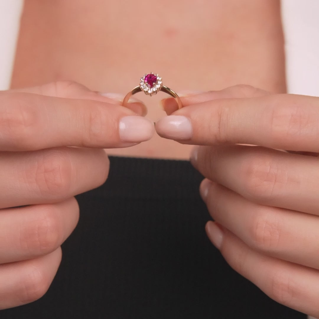 14K yellow gold pear shape ruby ring showcased by a woman, featuring a round ruby center and CZ side stones.