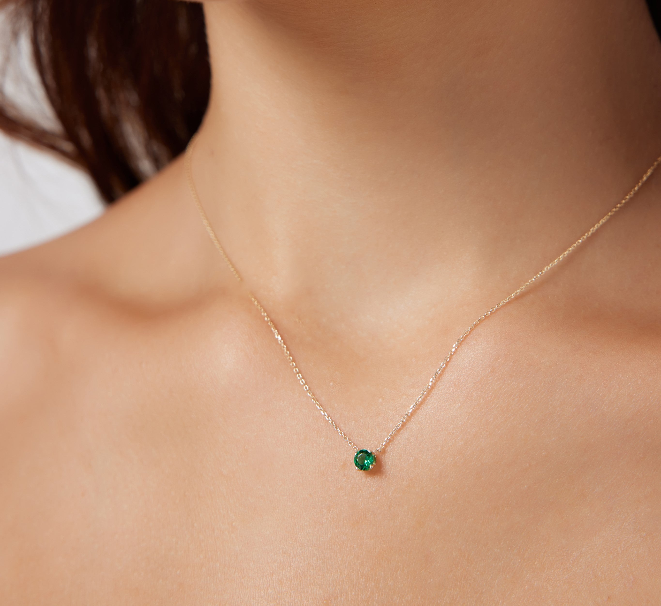 14K yellow gold minimalist solitaire emerald necklace on a model's neck, featuring a 5mm prong setting for a dainty look.