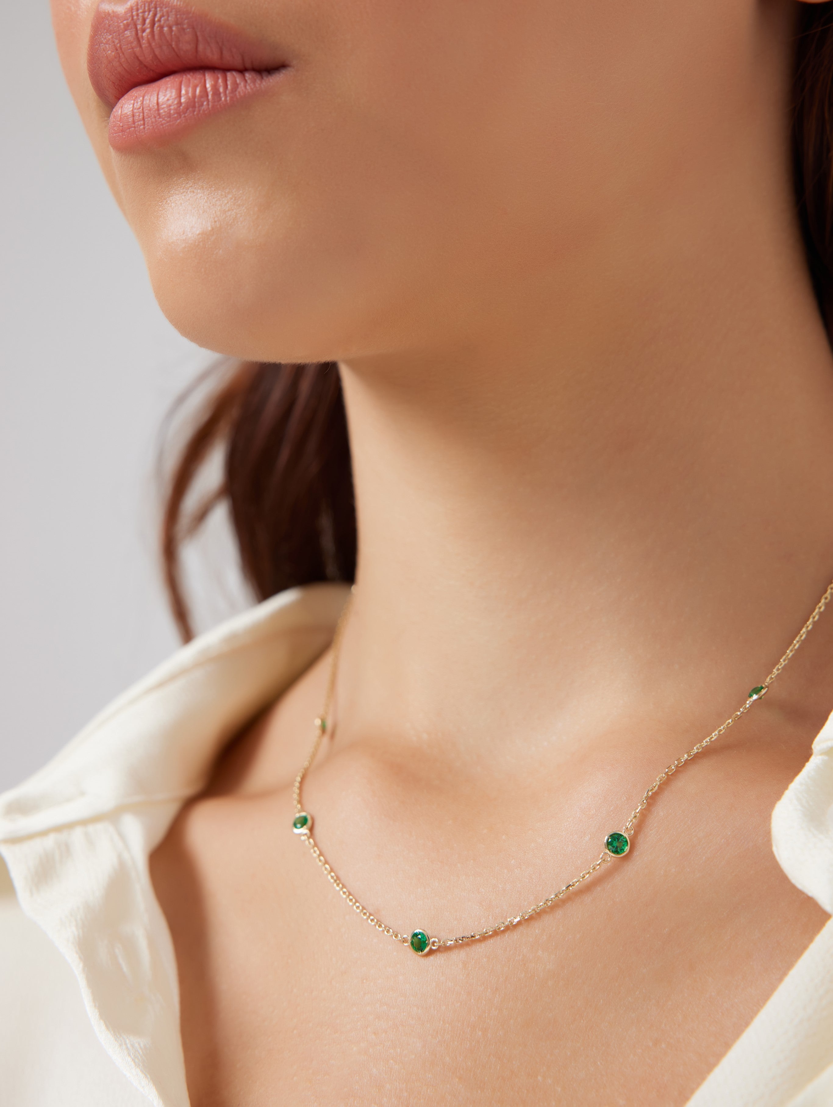 Model showcasing a 14K gold emerald station necklace, featuring delicate emerald gemstones in a stylish design.