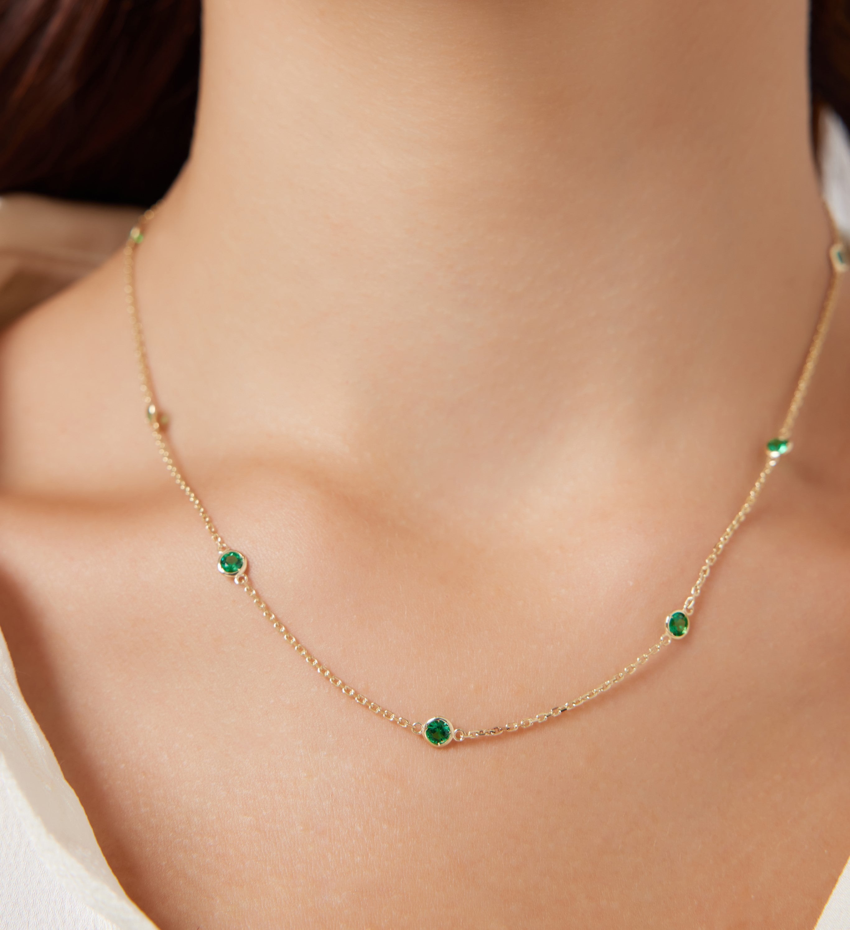 14K gold emerald station necklace worn on neck, featuring delicate emerald gemstones in a simple design.