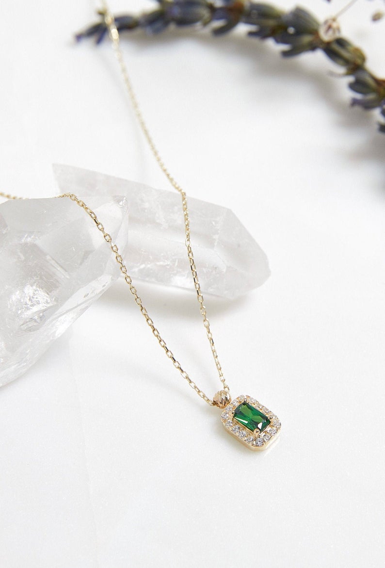 14K yellow gold emerald cut solitaire emerald necklace on a delicate chain among crystal pieces.