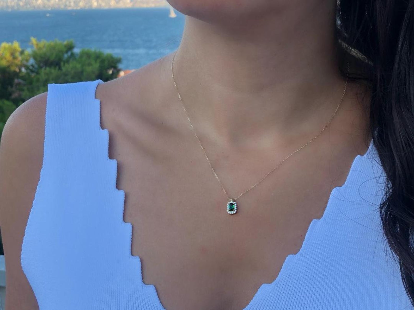Model wearing a 14K yellow gold emerald cut solitaire emerald necklace by the sea, showcasing elegance and simplicity.
