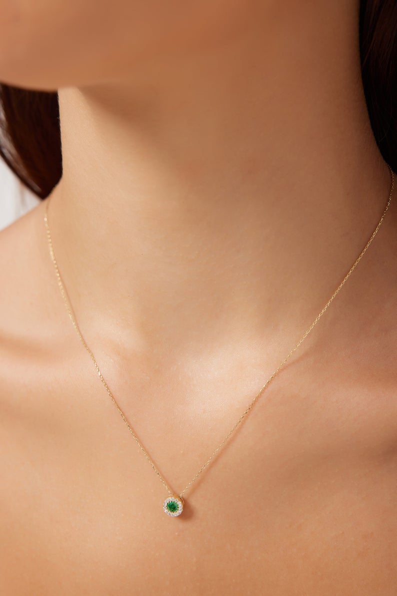 Minimalist 14K yellow gold necklace featuring a round solitaire emerald pendant on a model.