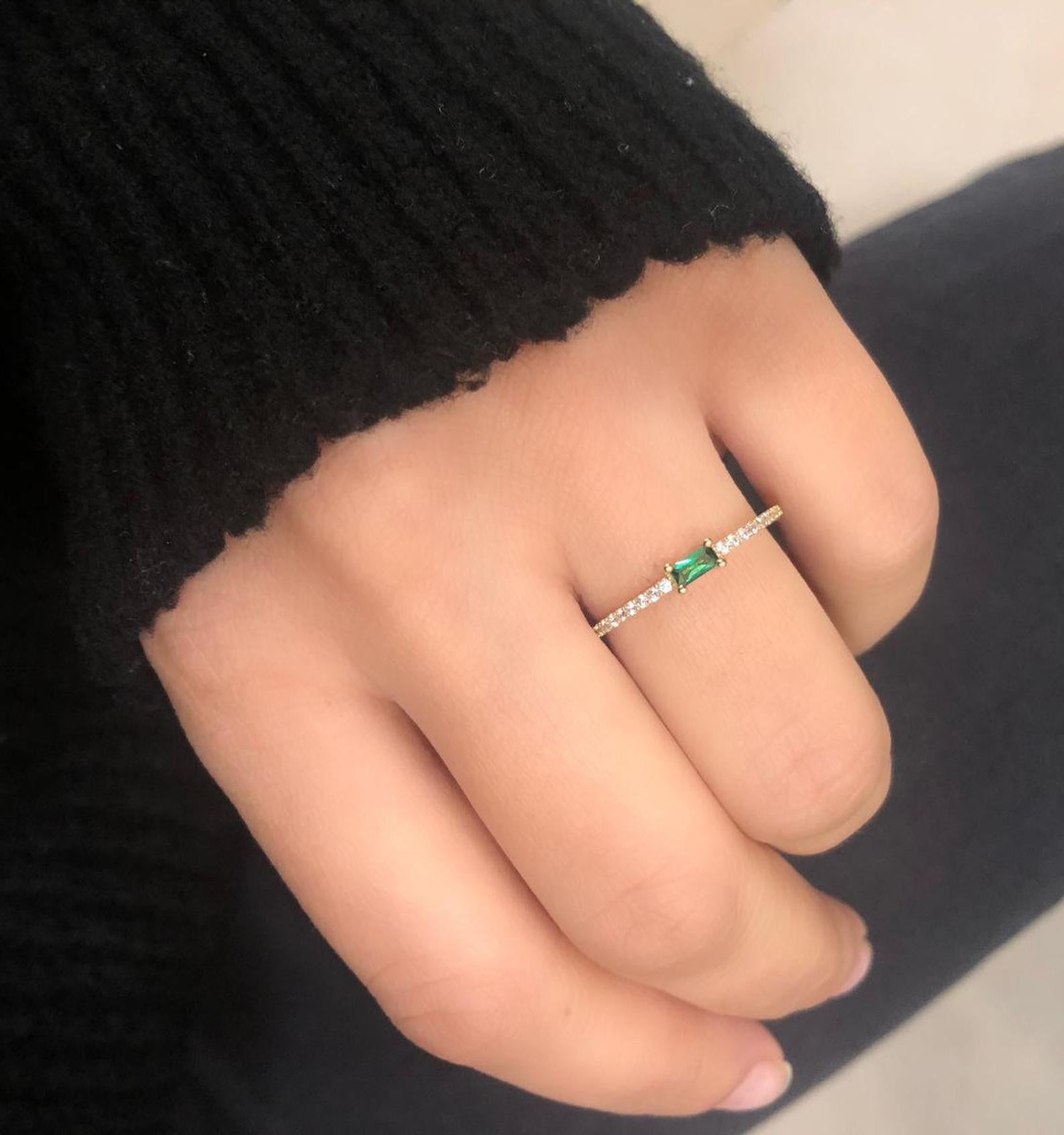 14K yellow gold minimalist wedding ring featuring a baguette emerald and diamond CZ, worn on a hand.