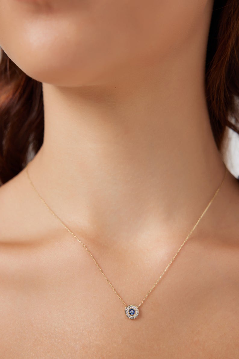 Minimalist 14K solid yellow gold round evil eye necklace on a model's neck, featuring a sparkling CZ detail.