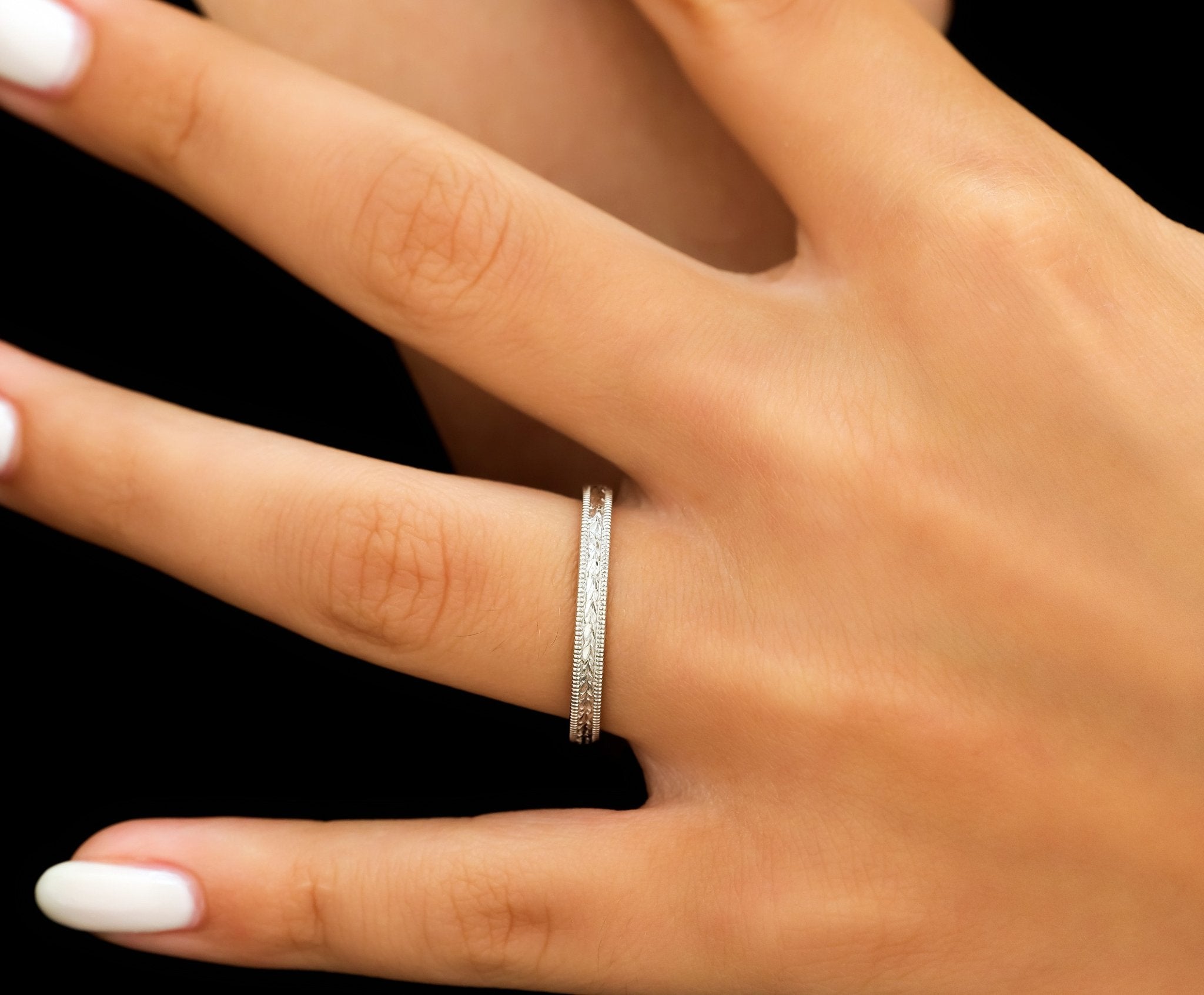 Hand engraved 10K white gold wedding band on a finger, featuring shiny finish and milgrain detail, 2.5mm wide.