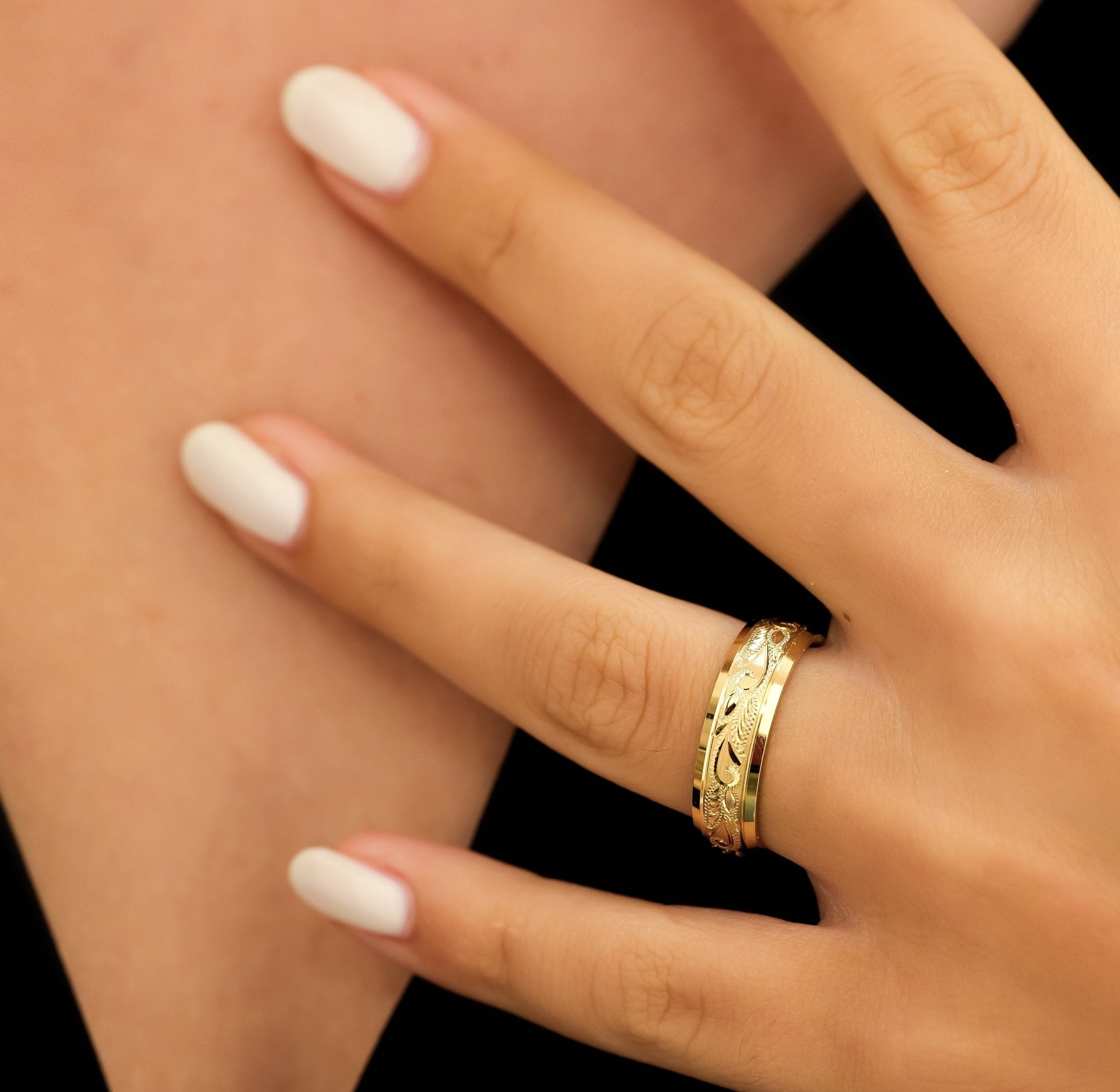Hand engraved mens wedding band in solid yellow gold, showcased on a model's hand with a beautiful shiny leaf motif design.