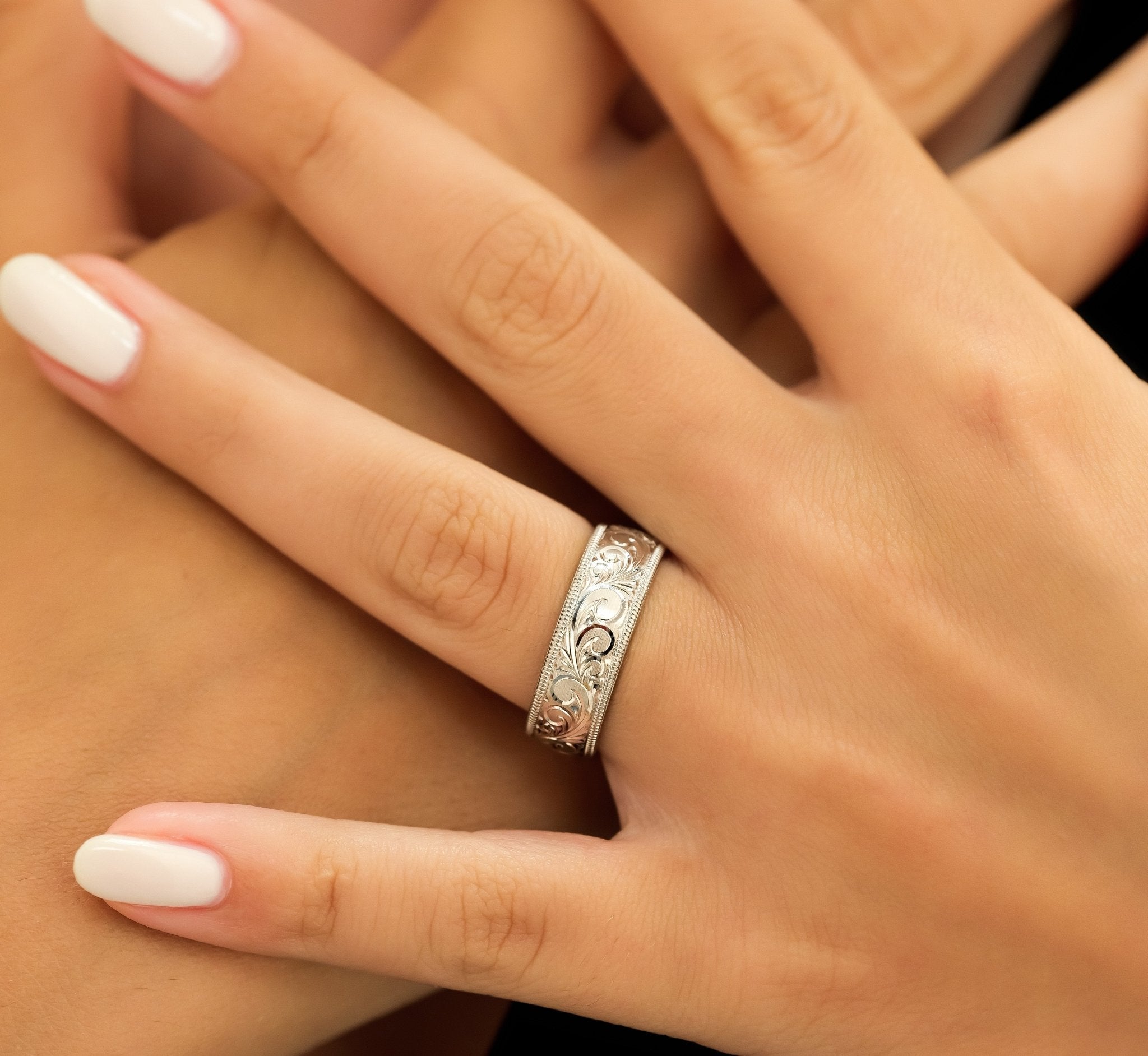Hand engraved 10K solid white gold wedding band with leaf motifs, 7mm wide, showcased on a hand.