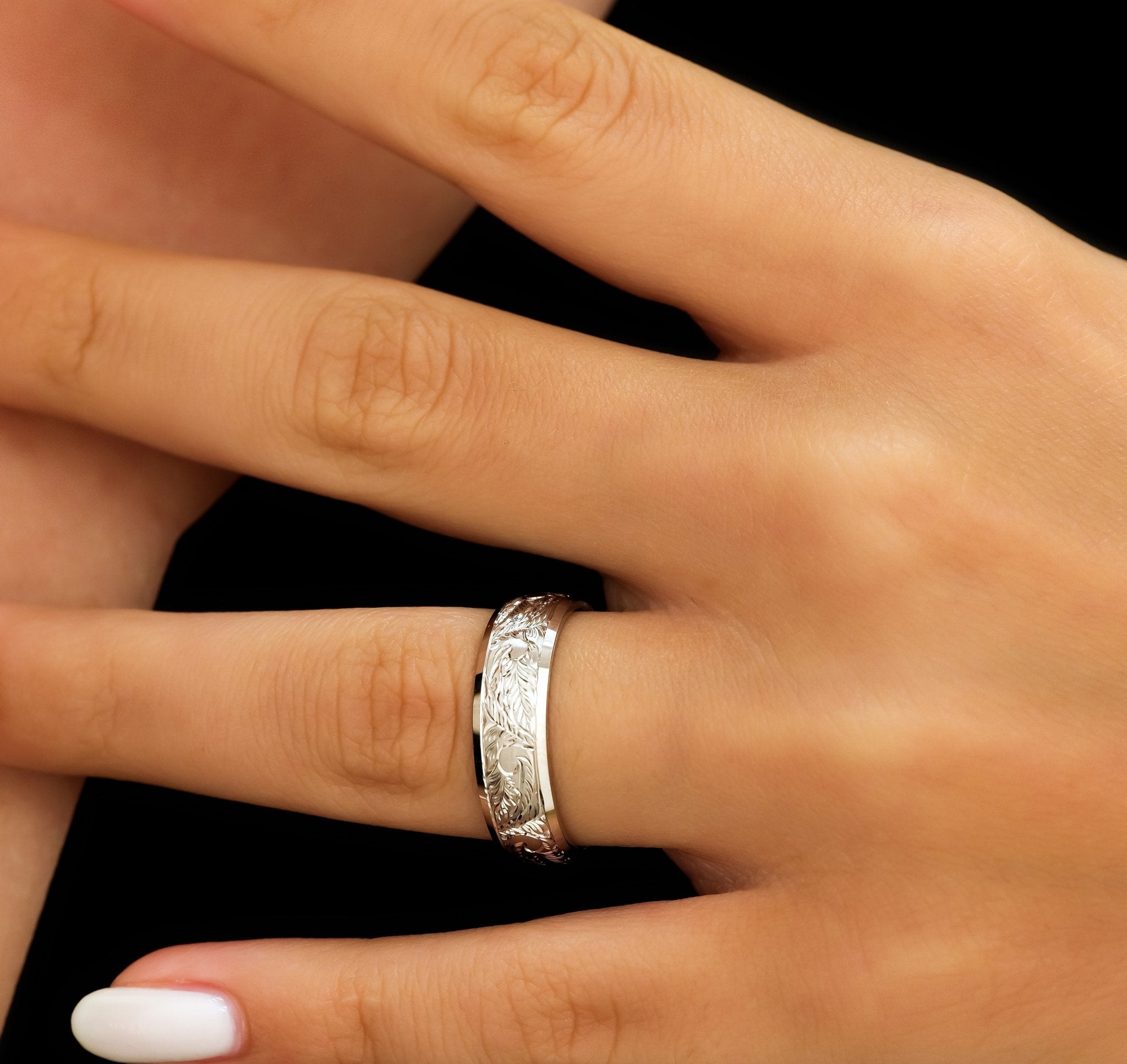 Hand engraved 10K white gold wedding band with leaf motifs, showcased on a hand against a black background.