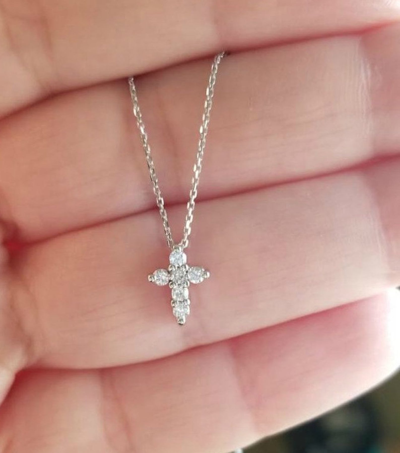 14K solid white gold minimalist diamond cross necklace held in hand, featuring sparkling diamonds.