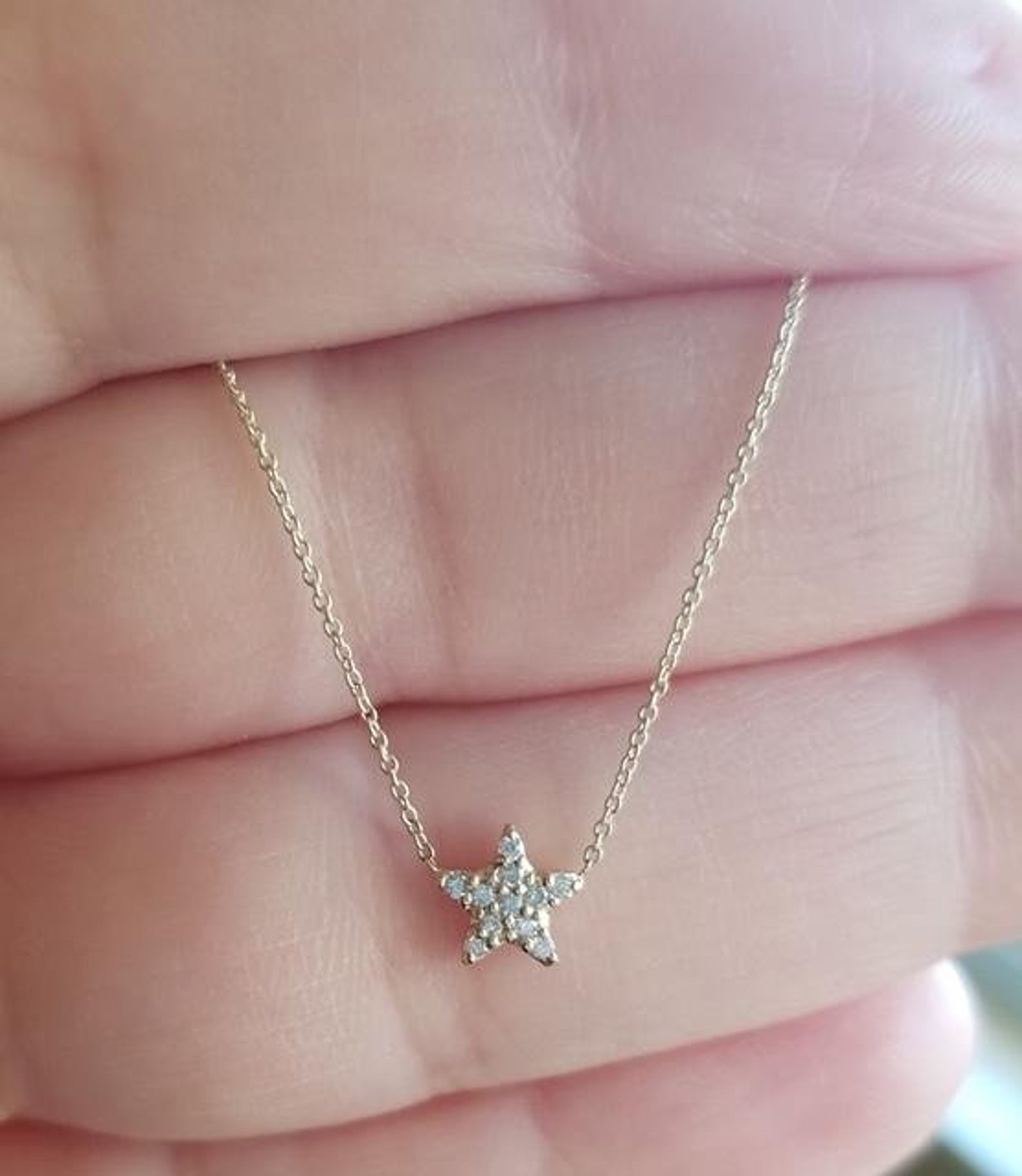 Dainty 14K solid white gold diamond star necklace held in hand, featuring sparkling G color diamonds.
