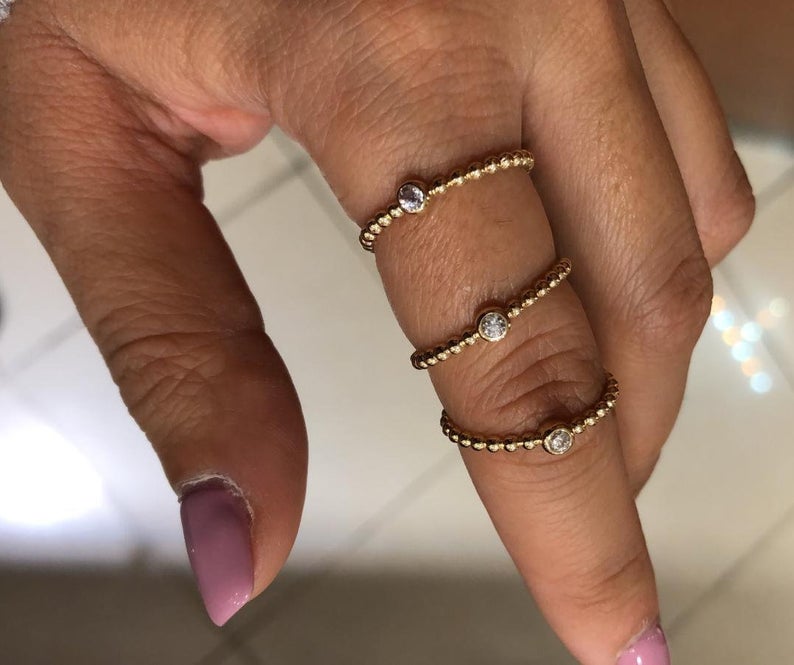Three 14K yellow gold minimalist rings with solitaire diamonds worn on a hand, showcasing elegant and modern style.