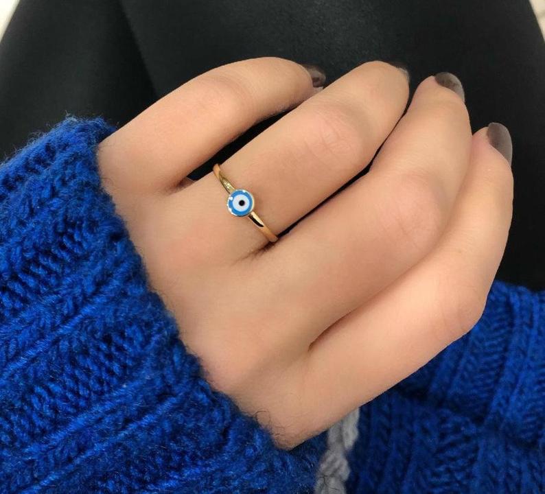14K solid yellow gold minimalist evil eye ring worn on hand with blue sweater.