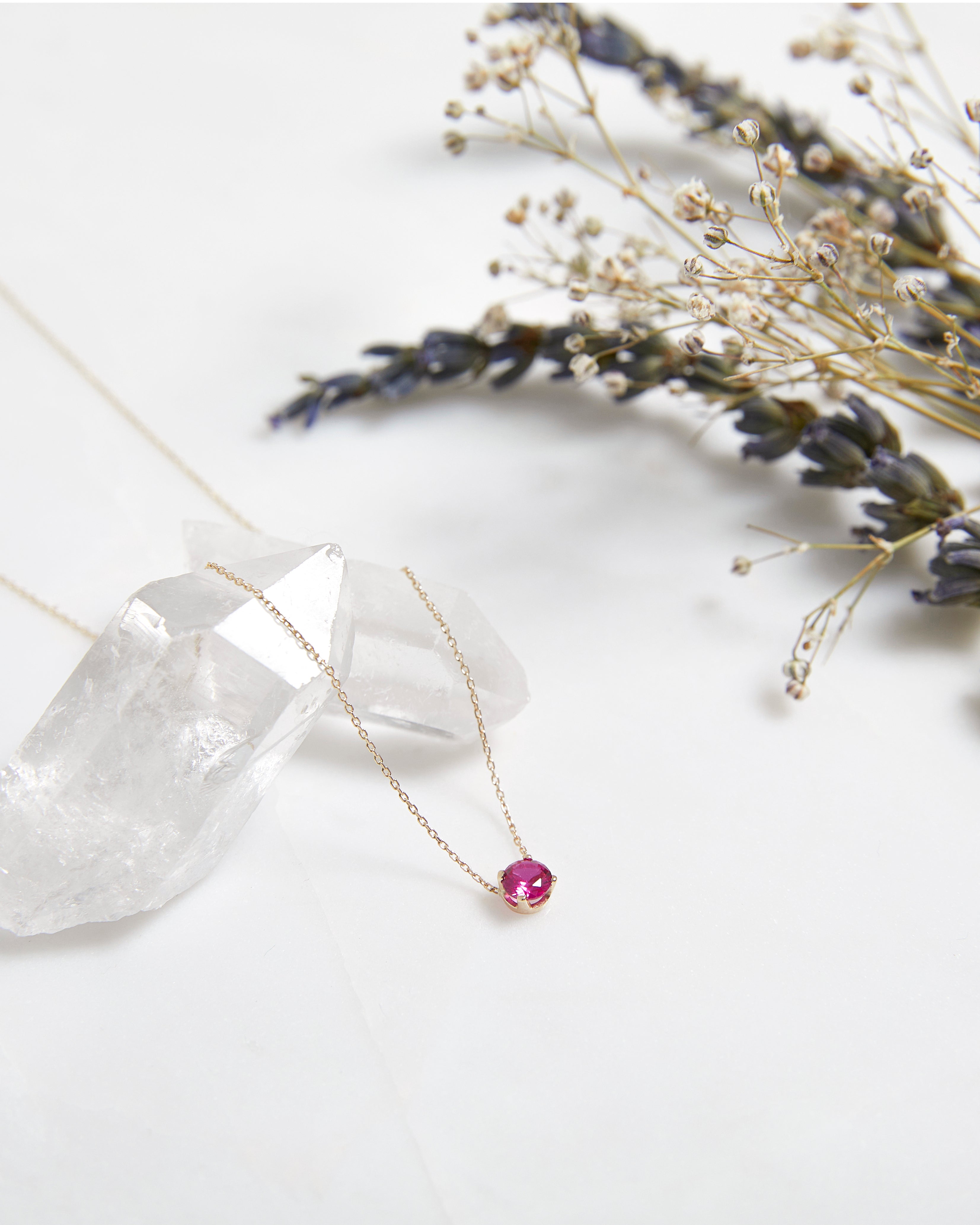 Dainty 14K yellow gold necklace featuring a 6mm lab-created ruby solitaire, surrounded by delicate flowers.