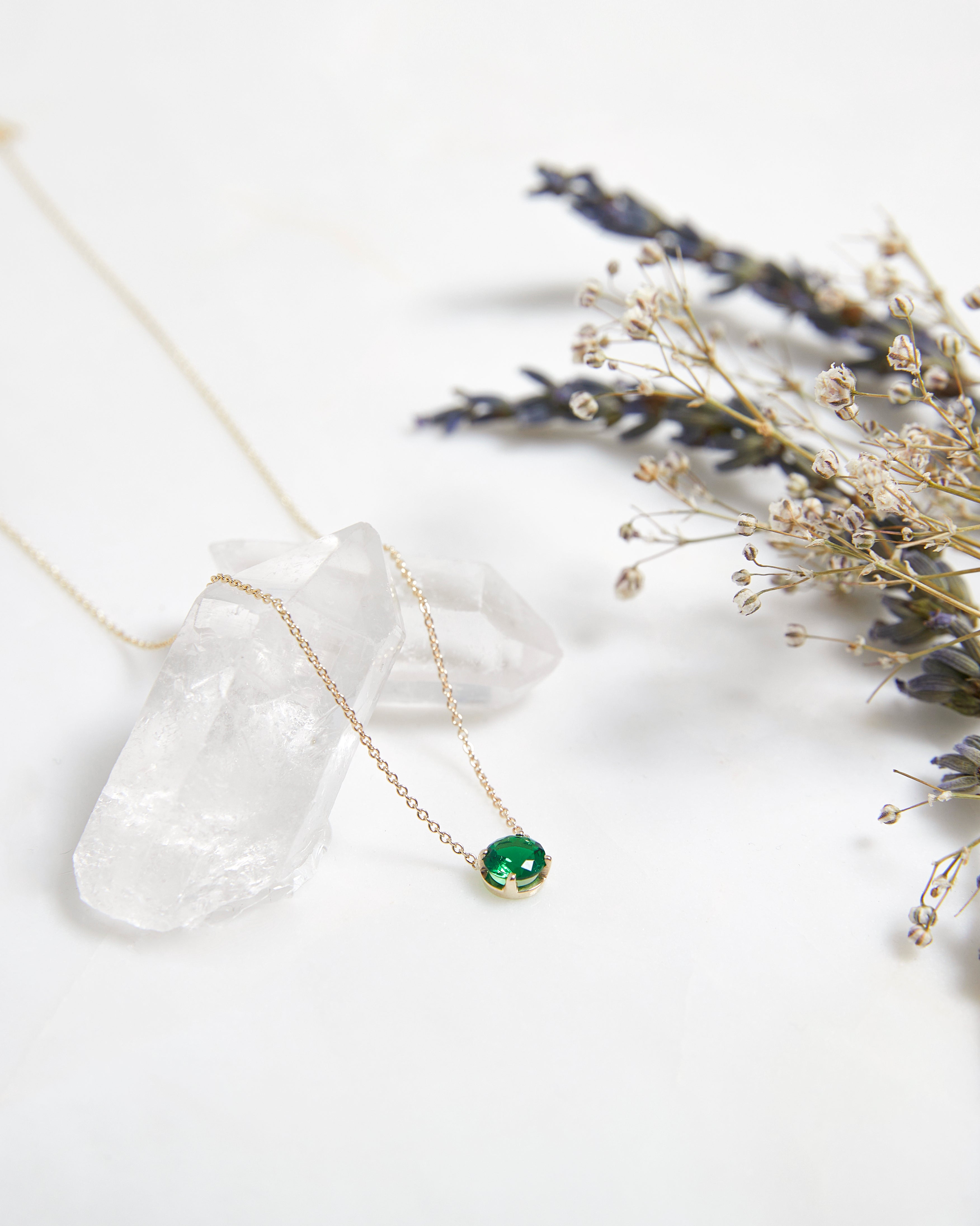 14K white gold 6mm prong setting solitaire emerald necklace on a crystal with dried flowers.