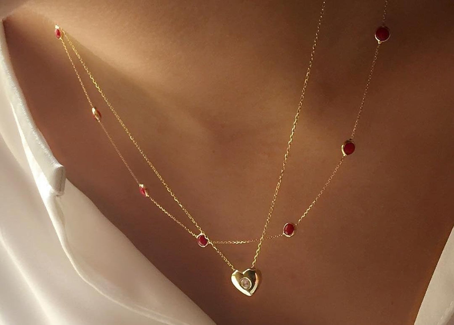 14K solid yellow gold beaded station ruby necklace showcased on a model, featuring delicate ruby accents and a heart charm.