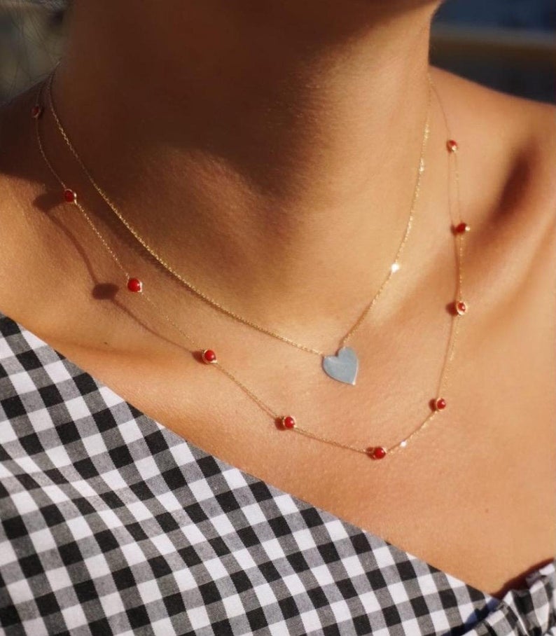 Model wearing a 14K solid yellow gold ruby station necklace with a heart pendant on a checked top.