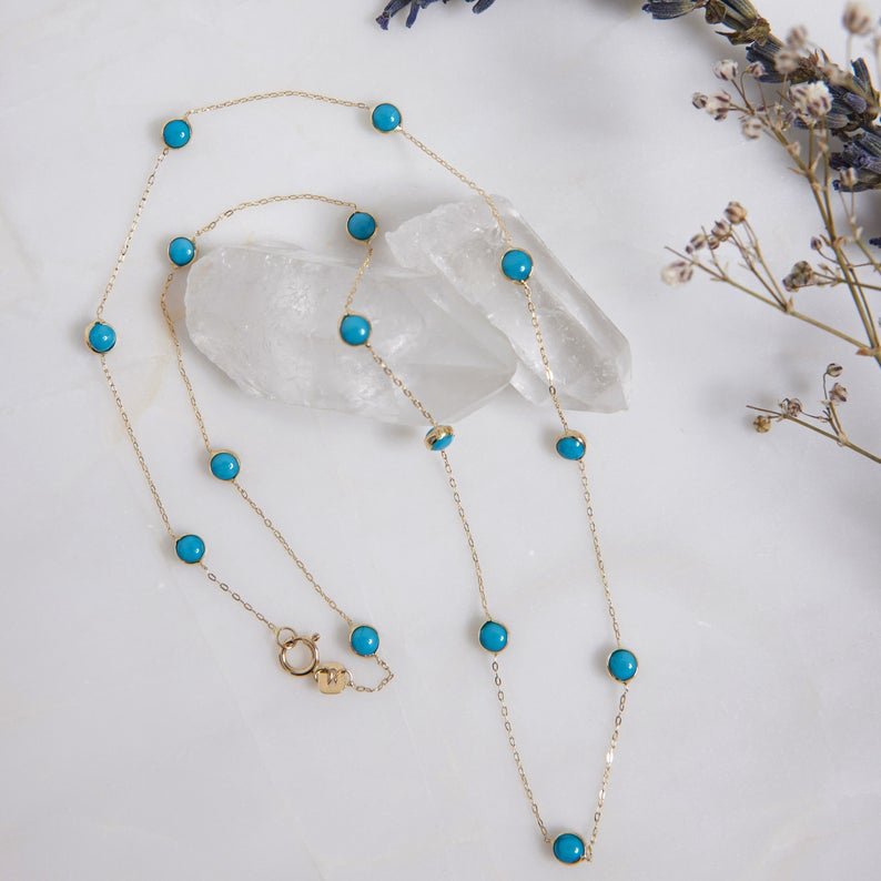 14K solid yellow gold beaded station turquoise necklace on a marble surface with crystal accents.
