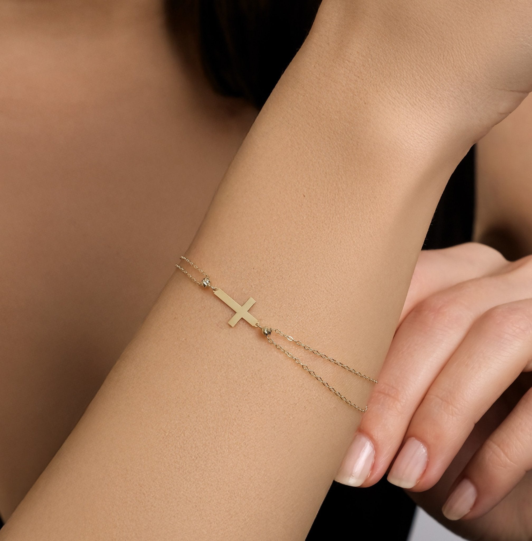 14K solid yellow gold small cross bracelet worn on wrist, showcasing dainty design and adjustable length.