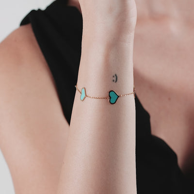 14K solid yellow gold station bracelet featuring turquoise heart charms, elegantly worn on a woman's wrist.