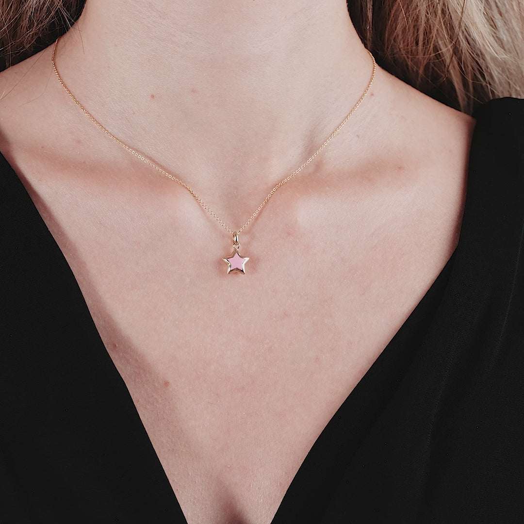 Close-up of a woman wearing a 14K yellow gold puffed pink star necklace, showcasing its elegance and charm.