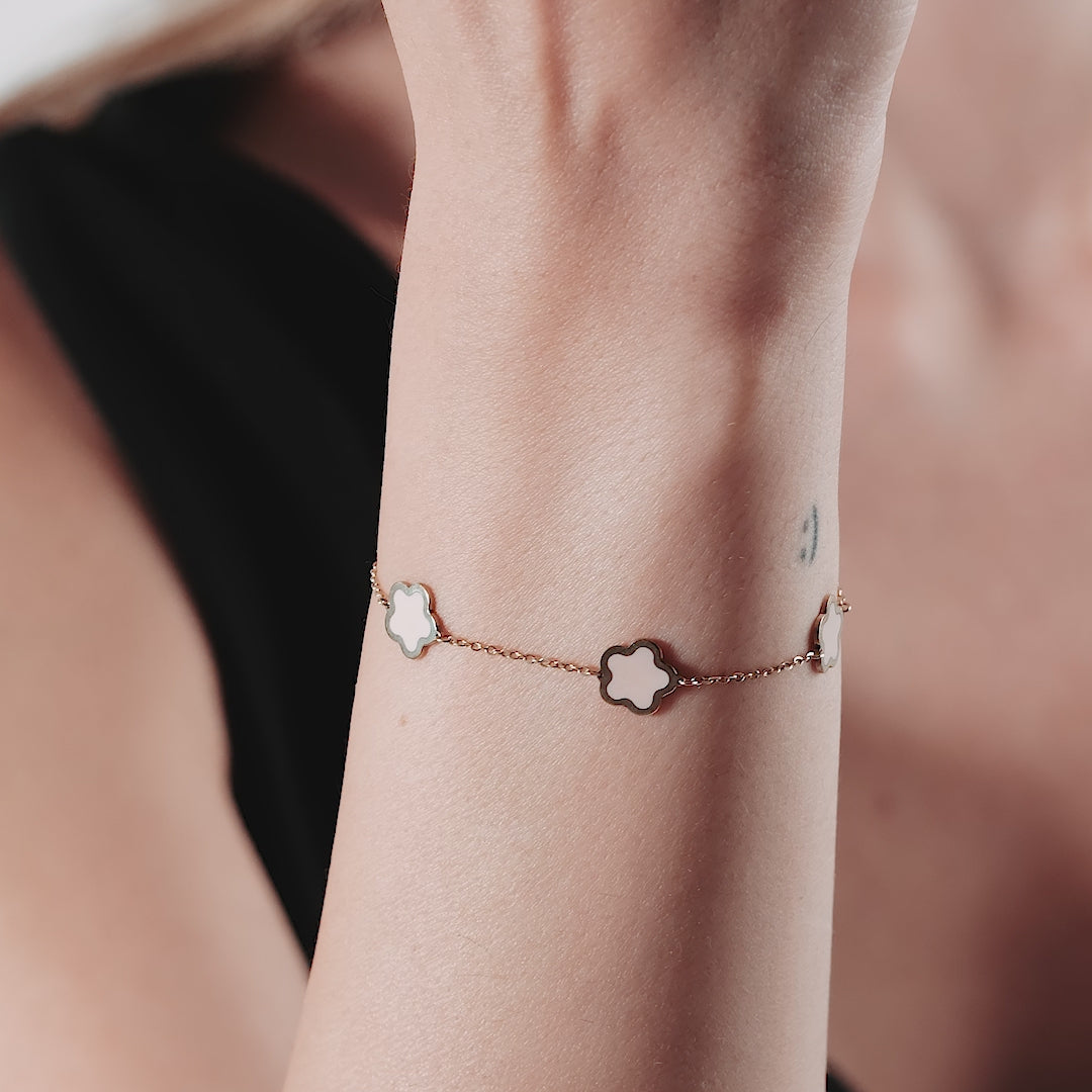 Close-up of a woman's wrist wearing a 14K yellow gold pink blossom bracelet with flower charms.