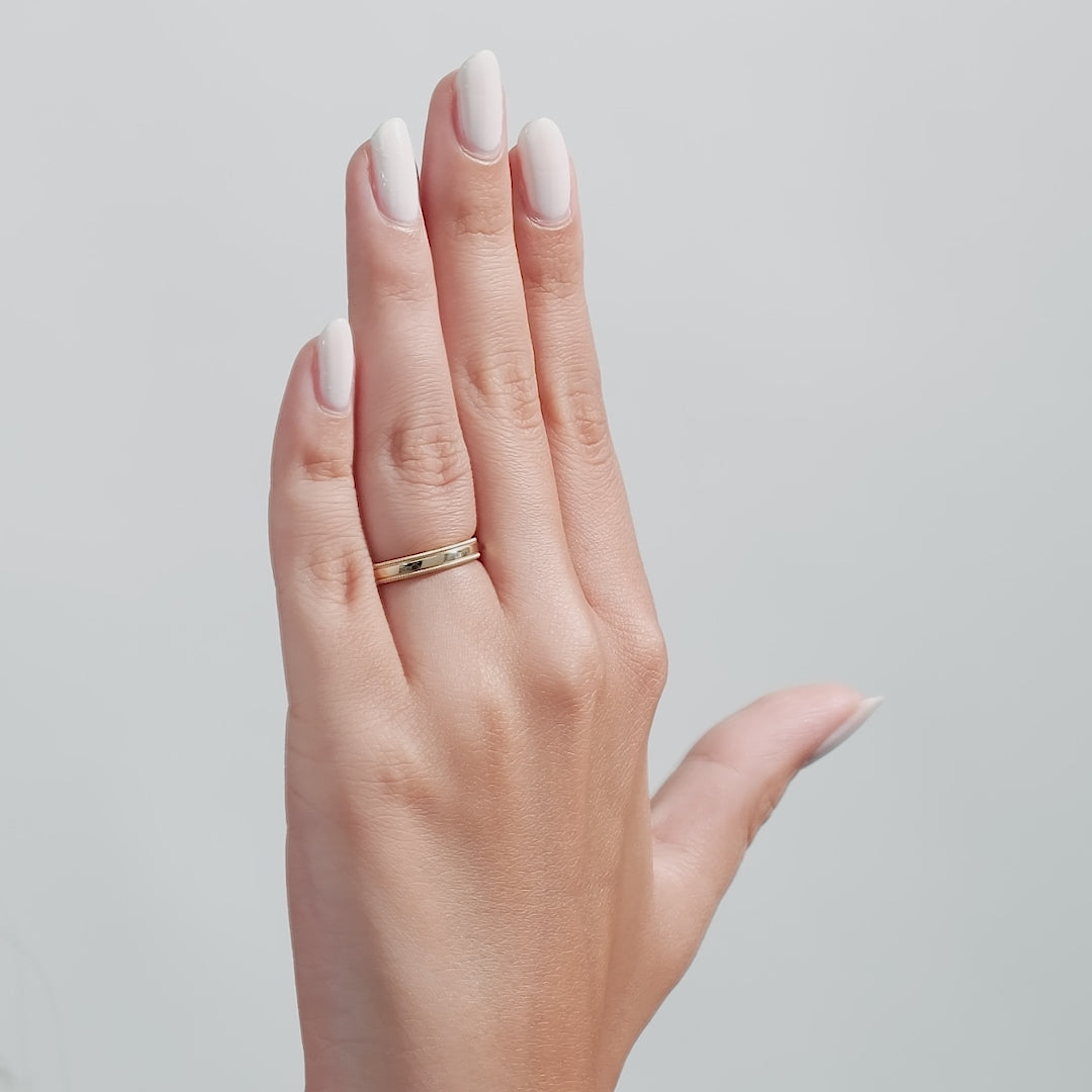 14K solid yellow gold beveled edge men's wedding band showcased on a woman's hand with manicured nails.