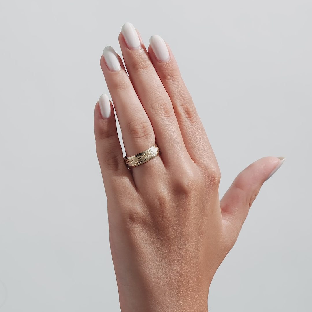 Hand wearing a hand engraved 10K gold wedding band with shiny leaf motifs, showcasing elegant design and comfort fit.