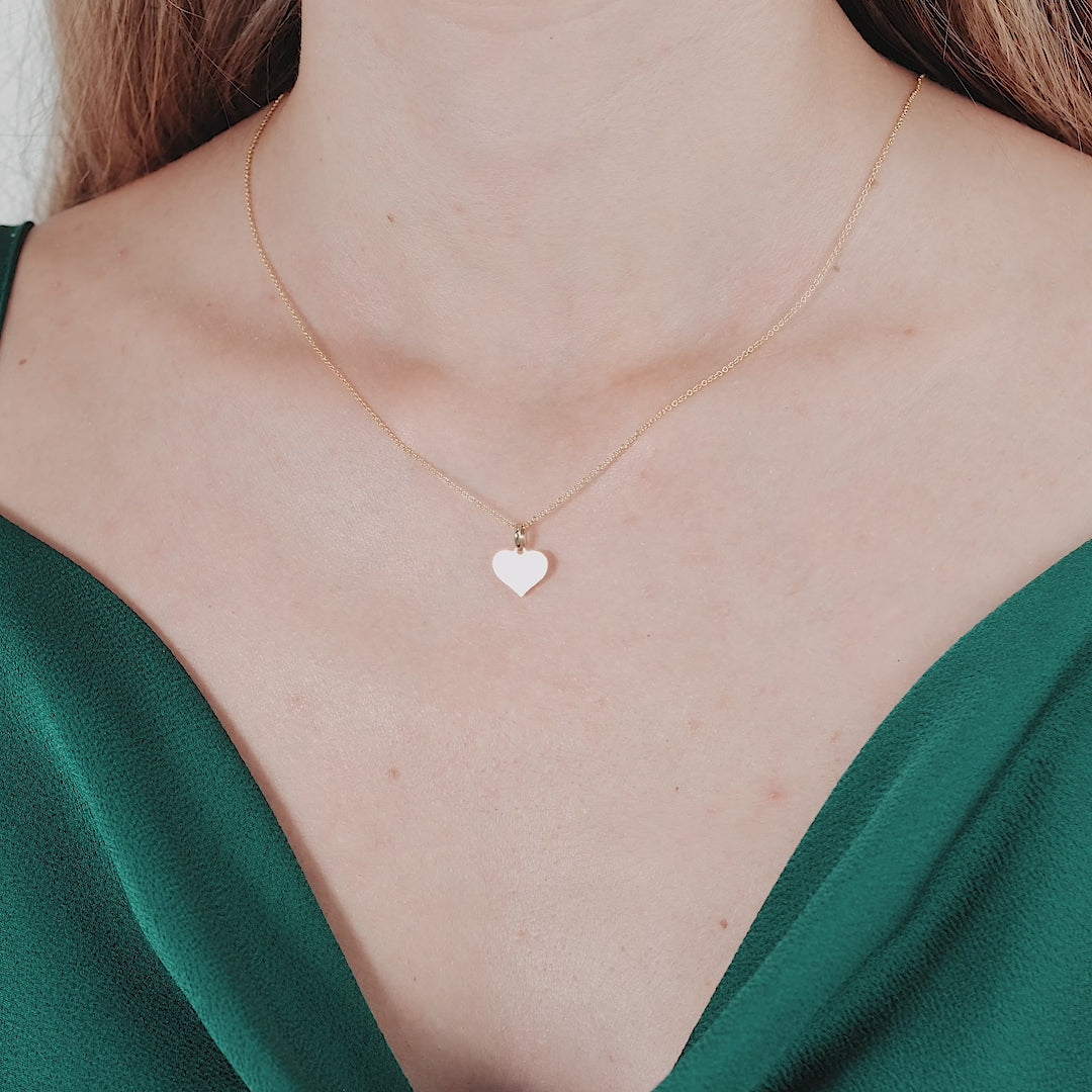 14K yellow gold flat mother of pearl heart pendant necklace worn by a woman in a green dress.