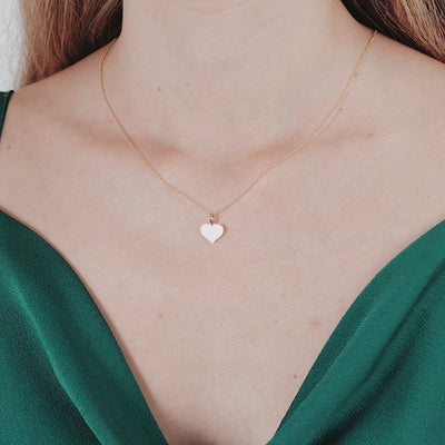 14K yellow gold flat mother of pearl heart pendant necklace worn by a woman in a green dress.