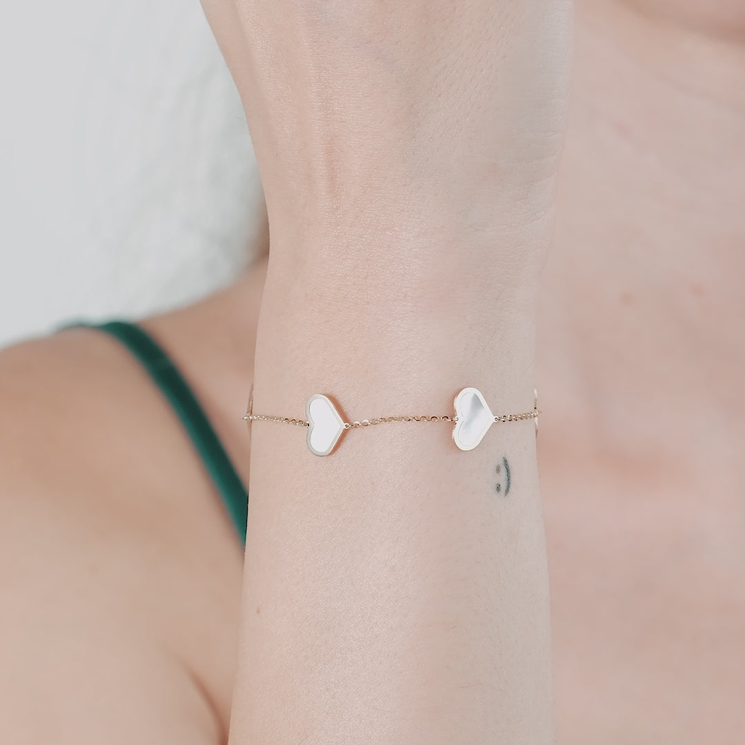 14K solid yellow gold bracelet with mother of pearl heart charms, elegantly worn on a woman's wrist.