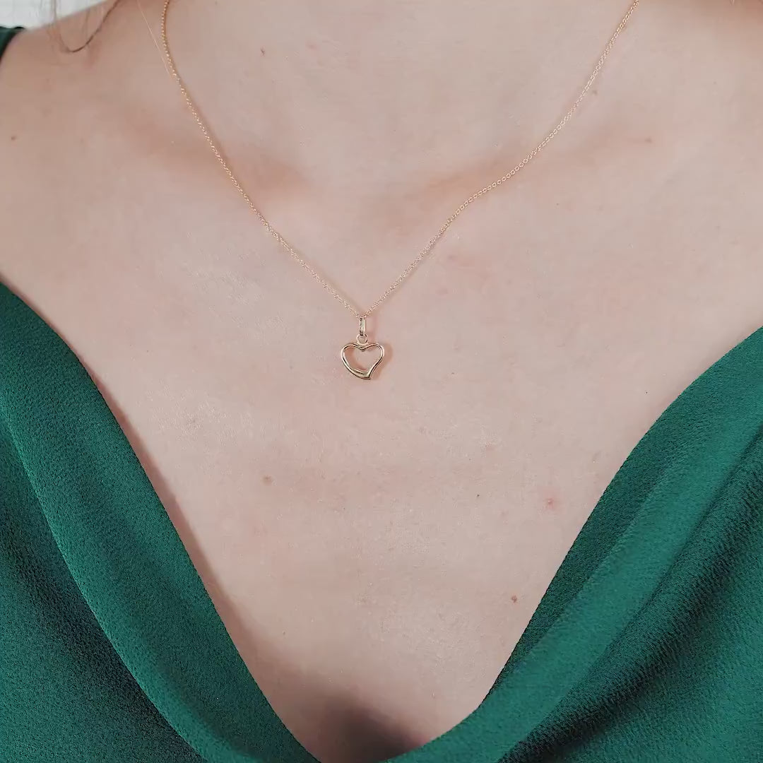 Dainty 14K yellow gold minimalist heart necklace worn around the neck with a green blouse.