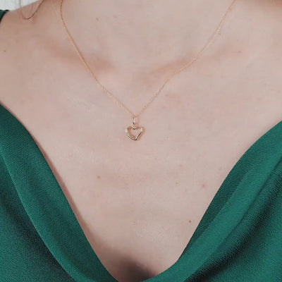 Dainty 14K yellow gold minimalist heart necklace worn around the neck with a green blouse.