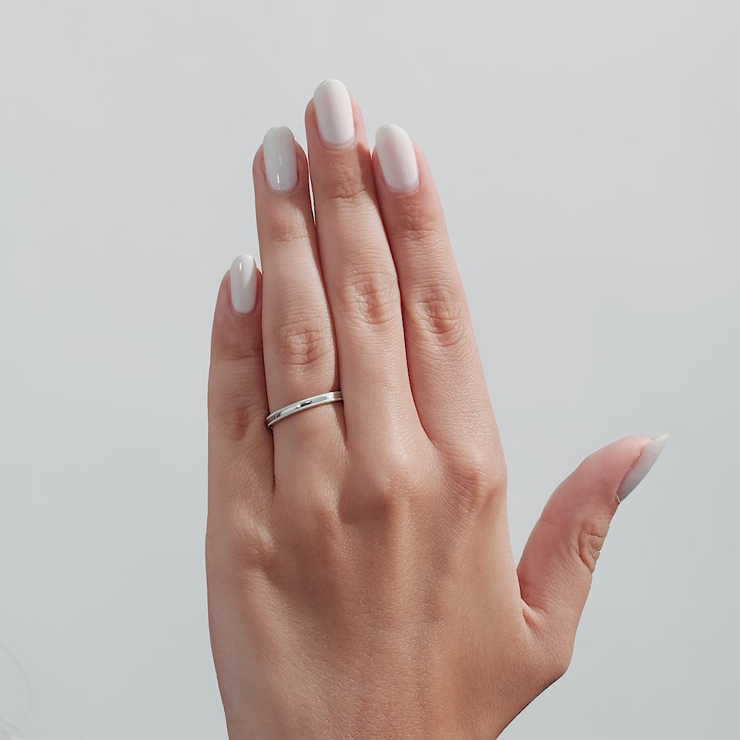 Dome milgrain platinum wedding band worn on a hand with manicured nails, showcasing its shiny finish and comfort fit.