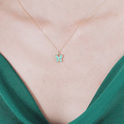 14K yellow gold butterfly pendant necklace with turquoise enamel, worn on a woman in a green dress.