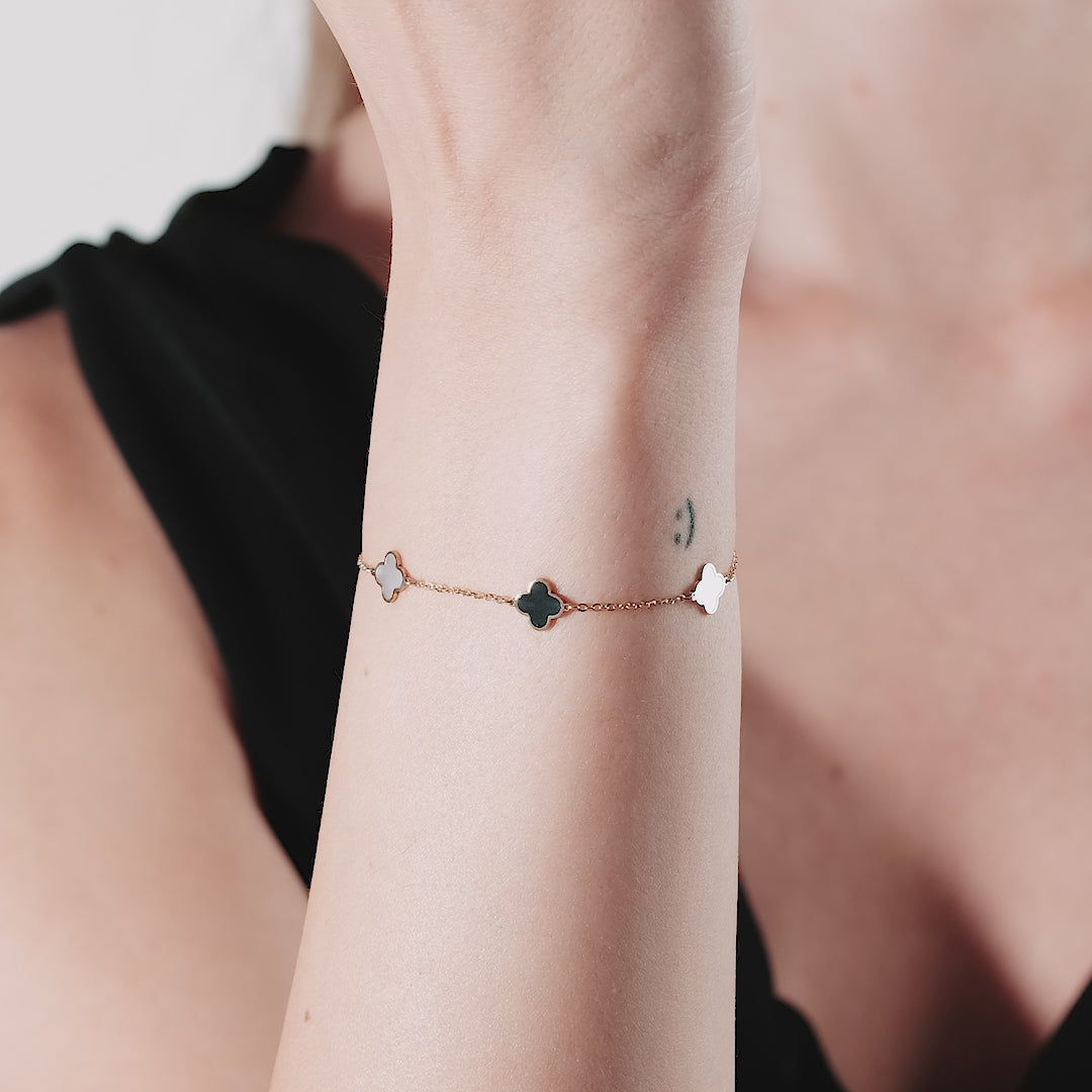 Dainty 14K solid yellow gold bracelet featuring mother of pearl and onyx four leaf clover design worn on wrist.