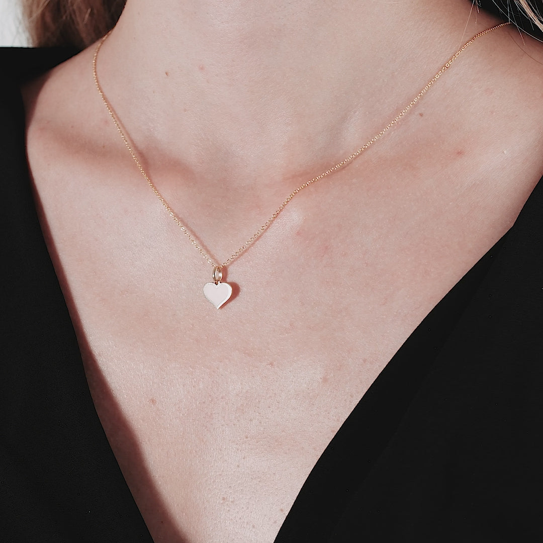 14K yellow gold flat pink heart necklace worn by a woman, showcasing its dainty design and elegance.