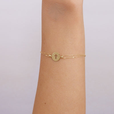 14K solid yellow gold small round disk cross bracelet worn on wrist, delicate design perfect for everyday use.
