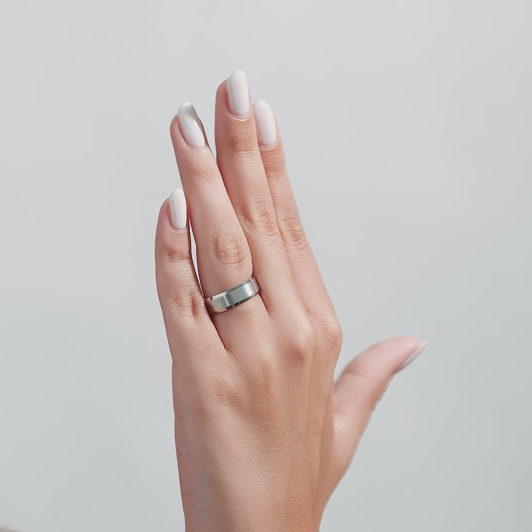 Woman's hand showcasing a 6mm white gold beveled edge wedding band with a satin and shiny finish.