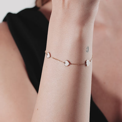 14K yellow gold minimalist bracelet with pink heart stations, worn on a wrist, showcasing elegant design and style.