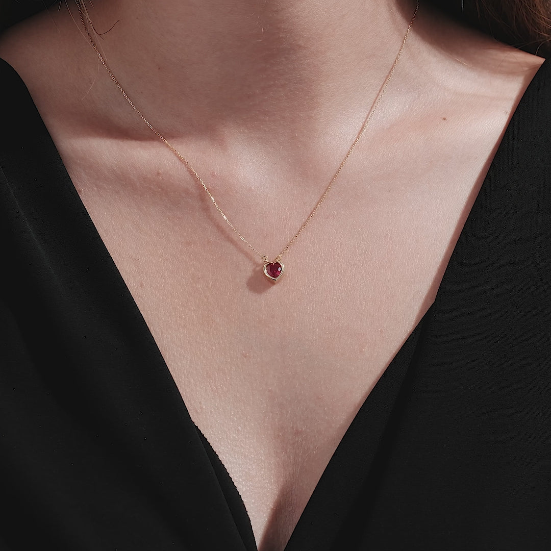 14K yellow gold heart shape solitaire ruby necklace worn elegantly, showcasing its stunning design against a dark outfit.