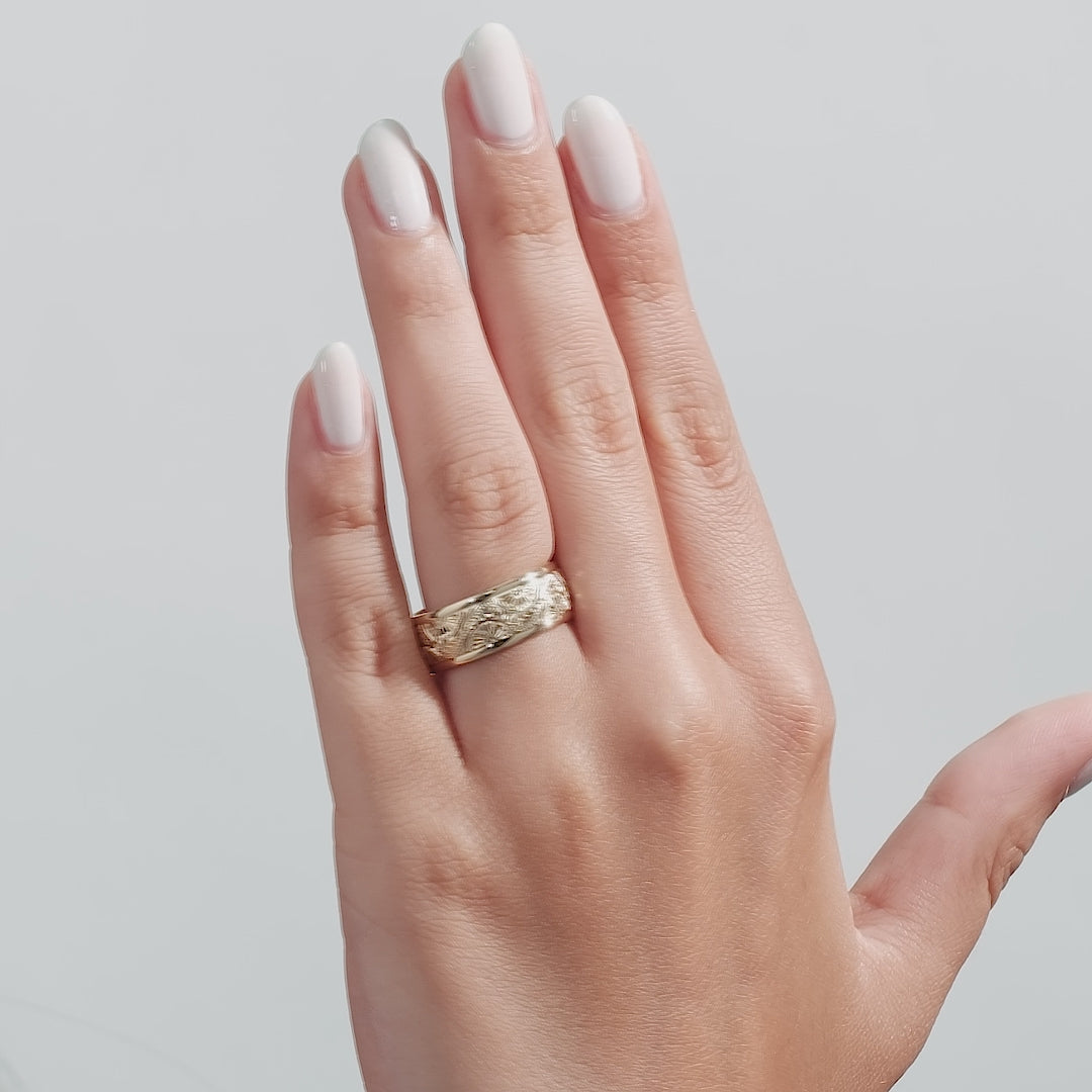 Hand engraved men's wedding band in solid yellow gold displayed on hand with shiny finish and leaf motif.