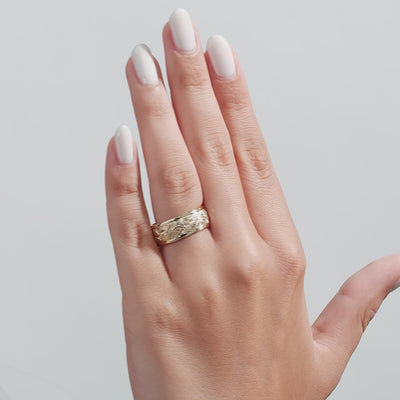 Hand engraved men's wedding band in solid yellow gold displayed on hand with shiny finish and leaf motif.