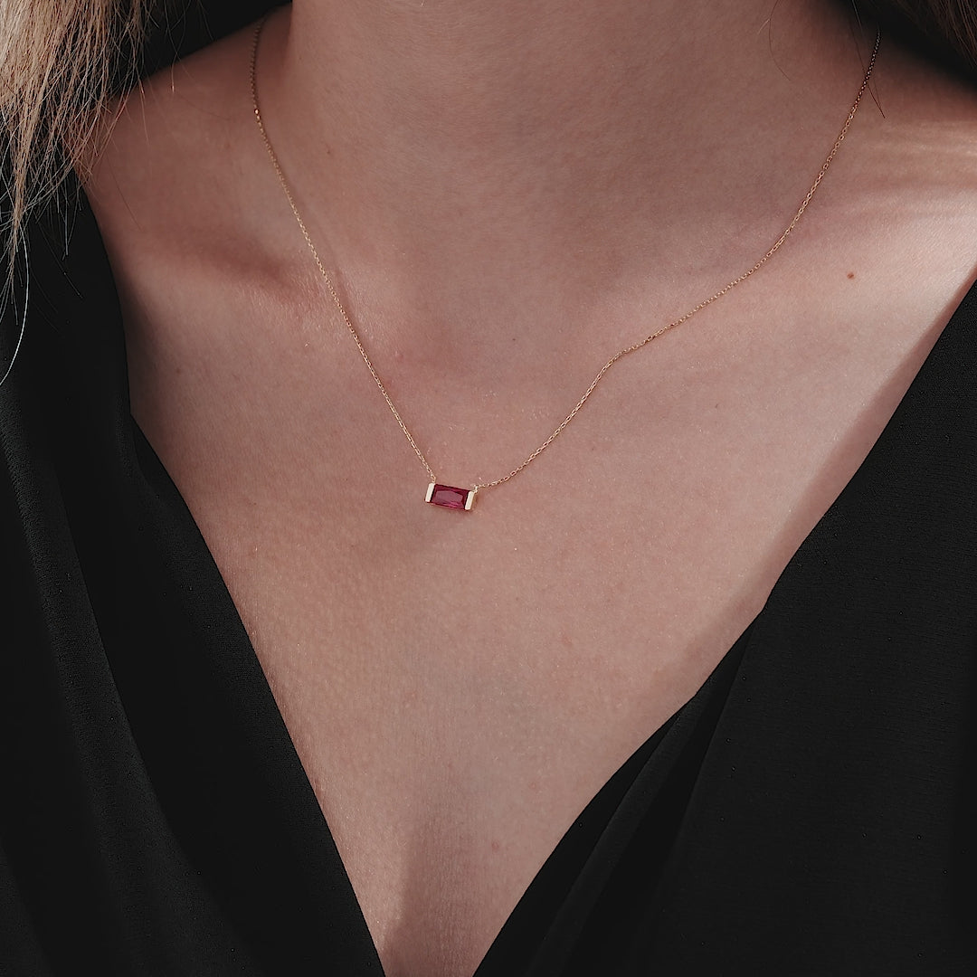 Delicate 14K yellow gold baguette ruby solitaire necklace worn on a model's neck, showcasing its minimalist elegance.
