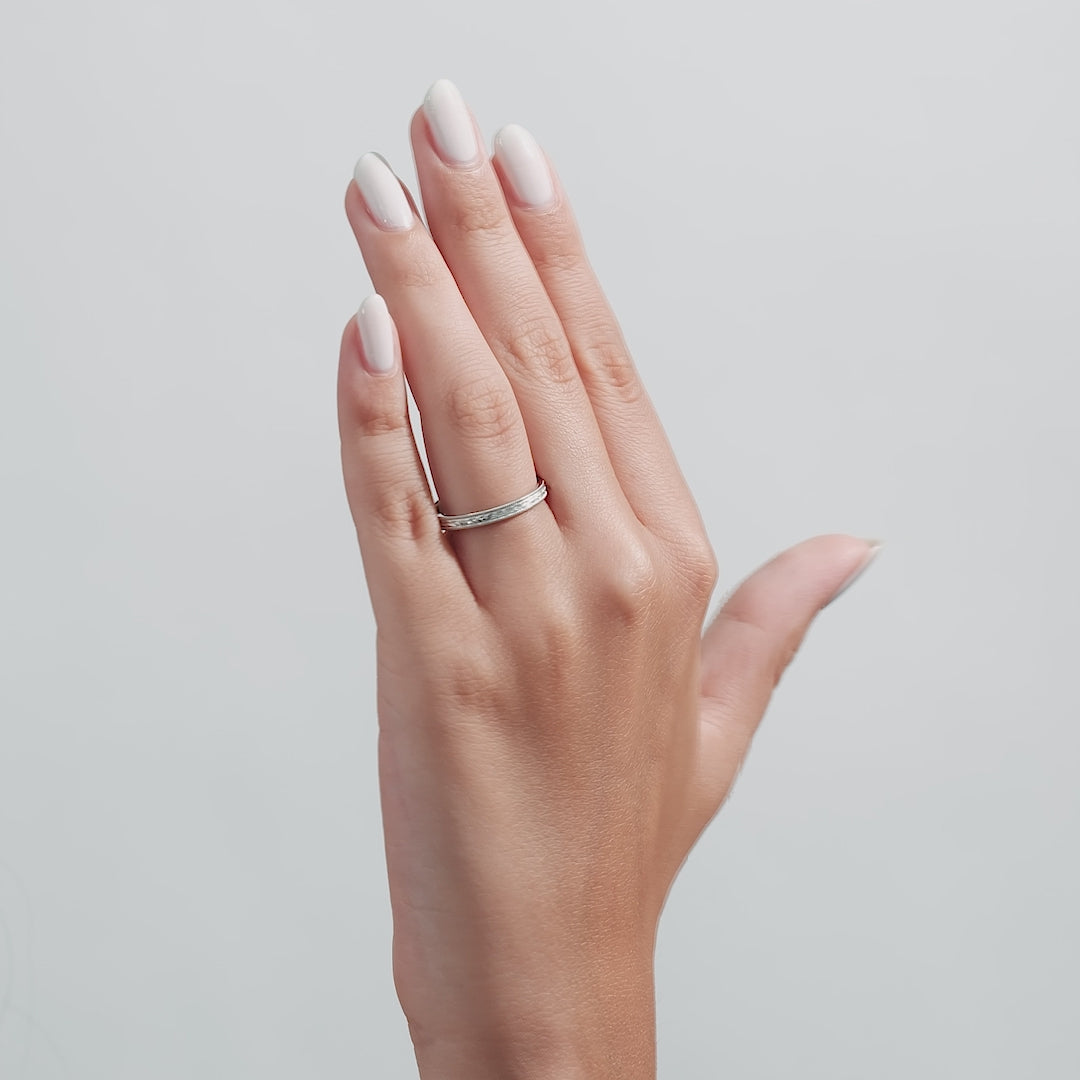 Hand wearing a hand engraved solid white gold wedding band, showcasing its shiny finish and milgrain design.