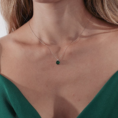 Close-up of a woman wearing a 14K white gold emerald solitaire necklace on a green dress.